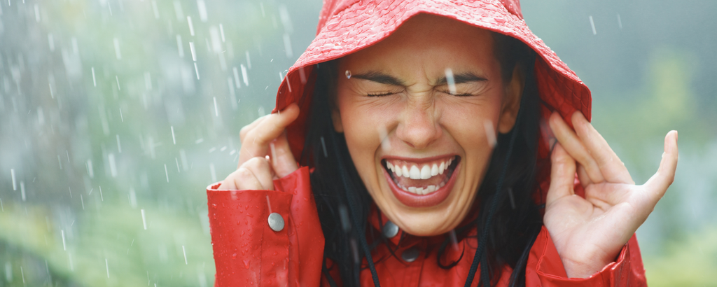 Lachende Frau mit roter Regenjacke im Regen stehend